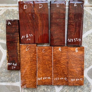 May include: Nine rectangular wooden blocks arranged in a grid, featuring varied wood grain patterns and glossy finishes. The blocks are labelled with letters A, B, C, D, and E, and include handwritten numerical measurements in millimetres on their surfaces.
