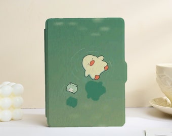 May include: A rectangular green e-reader case featuring a printed illustration of a small yellow duckling and a tiny green frog swimming in water. The design includes light ripples around the characters and dark green patches representing shadows.