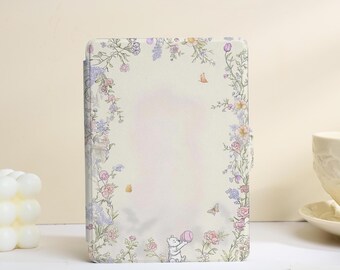 Peut inclure: Une housse de tablette rectangulaire sur fond crème, ornée d'une bordure florale délicate composée de vignes roses, violettes et vertes. Une petite illustration d'un ours tenant un ballon rose est située au centre en bas de la couverture.
