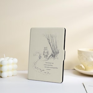 May include: A cream-coloured e-reader case featuring a black line-art illustration of Winnie the Pooh and Piglet walking away. The text reads, "How lucky I am to have something that makes saying goodbye so hard." The case has a black edge and frame.