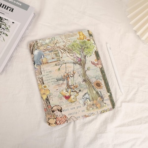 Może przedstawiać: Przezroczyste etui na tablet z kolorową ilustracją Kubusia Puchatka i jego przyjaciół. Projekt zawiera postacie takie jak Puchatek, Tygrysek i Kłapouchy, z tekstem z opowieści. Etui leży na białej powierzchni.