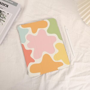 May include: A colorful tablet case with a playful design. The case features abstract shapes in pastel colors including pink, orange, yellow, green, and blue. A white stylus rests beside the case.
