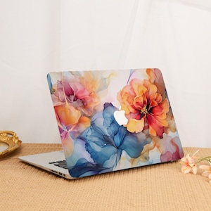 Può includere: Un computer portatile dotato di una cover protettiva con un design floreale astratto ad acquerello nei toni dell'arancione, rosa, blu e giallo. Il design mostra grandi forme di petali fluidi sulla superficie, con il logo Apple visibile al centro.