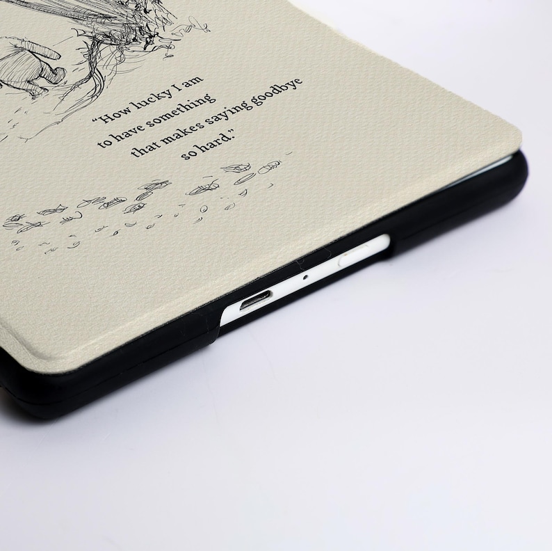 May include: A cream-coloured tablet case with a black frame featuring a line-art illustration of a character and the text, "How lucky I am to have something that makes saying goodbye so hard." The case has a textured surface and a visible charging port.