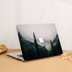 Può includere: Un computer portatile con una scena di montagna nebbiosa in bianco e nero sulla copertina. Il logo Apple è visibile sulla copertina.