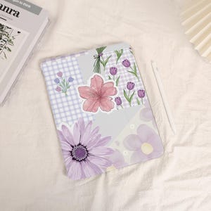 Può includere: Una custodia per tablet a tema floreale, con un design patchwork con una grande margherita viola, un fiore rosa e tulipani viola. La custodia presenta un motivo a quadri viola chiaro e bianco e uno stilo bianco.