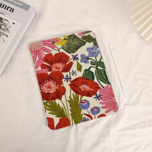 May include: A rectangular tablet case featuring a cream background with a vibrant floral pattern of large red poppies, pink daisies, small blue flowers, and green leaves. A white stylus is positioned to the right of the tablet case.
