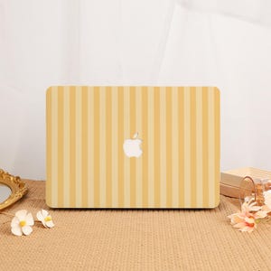 May include: A rectangular laptop skin featuring a vertical striped pattern in alternating shades of light yellow and soft cream. The design includes a central cutout revealing the white Apple logo, providing a clean and uniform aesthetic for the device.