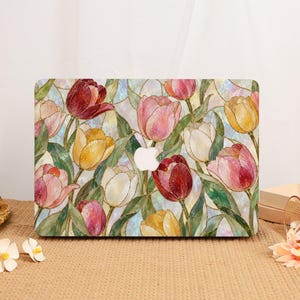 Peut inclure: Un autocollant pour ordinateur portable arborant un motif de vitrail représentant des tulipes dans des tons de rouge, rose, jaune et blanc avec des feuilles vertes. Le design inclut une découpe centrale pour le logo Apple sur un fond irisé.