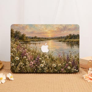 Può includere: Una custodia rigida per laptop con un paesaggio dipinto a olio raffigurante un fiume al tramonto, circondato da un campo di margherite bianche e fiori selvatici viola. L'iconico logo Apple bianco è visibile al centro del coperchio.