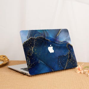 May include: A laptop with a blue and gold abstract design. The design features swirling shades of blue with gold accents. The Apple logo is visible on the laptop's cover. The laptop is open, displaying the keyboard.