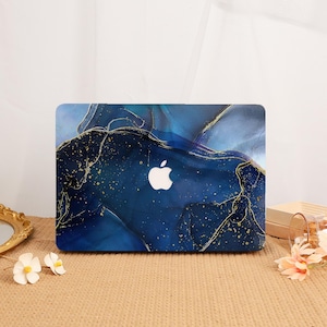 May include: A laptop hard shell case featuring a deep blue and navy marble-like pattern with swirling ink effects. The design includes thin, shimmering gold veins and scattered gold flecks throughout, with a central cutout for the Apple logo.
