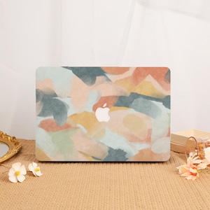 May include: A laptop hard shell case featuring an abstract watercolor pattern with blended shades of muted orange, soft blue, sage green, and cream. The design includes a central cutout revealing the silver Apple logo on the laptop surface.