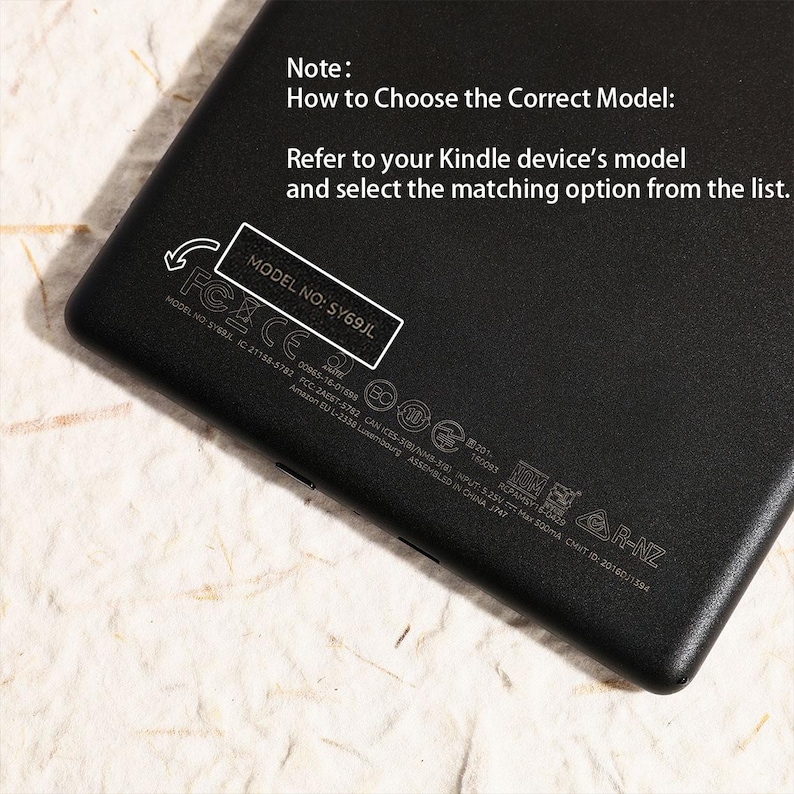 May include: A black electronic device back panel featuring white printed text that reads: Note: How to Choose the Correct Model: Refer to your Kindle device's model and select the matching option from the list. A box highlights MODEL NO: SY69JL.