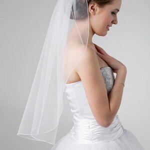 Op de afbeelding: Een witte bruids sluier van tule met een enkele laag, gedragen door een bruid in een witte bruidsjurk.