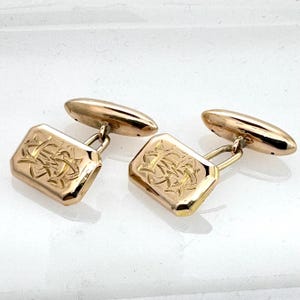 May include: A pair of gold cufflinks with an intricate engraved design. The cufflinks are rectangular in shape and have a polished finish.