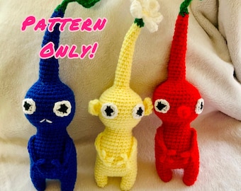 Puede incluir: Tres peluches de crochet con forma de los personajes del videojuego Mother 3. Los peluches son azules, amarillos y rojos. El texto "PATTERN ONLY!" está escrito en letras rosas en la imagen.