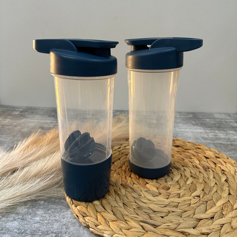May include: Two navy blue shaker bottles with clear plastic bodies and black mixing balls. The bottles have a flip top lid and a carrying handle.