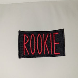 May include: Black fabric patch with red embroidered text that reads "ROOKIE".
