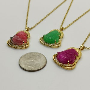 May include: Three gold necklaces with pendants featuring a smiling Buddha figure carved from green, pink, and red jade. The pendants are surrounded by small clear stones.