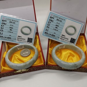 K&ouml;nnte beinhalten: Zwei Jadeit-Armreifen in ihren individuellen Schachteln. Jede Schachtel enth&auml;lt ein Echtheitszertifikat mit dem Gewicht, der Farbe, der Dichte und der Identifikationsnummer des Armbands. Die Zertifikate sind in Chinesisch.