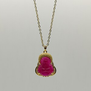 May include: A gold chain necklace with a pink jade pendant featuring a carved image of a Buddha. The pendant is surrounded by small clear stones.