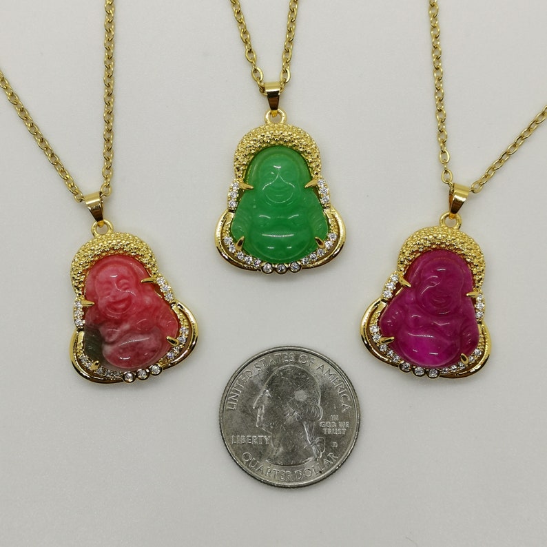 May include: Three gold necklaces with pendants featuring a smiling Buddha figure. The pendants are made of green, pink, and red jade and are surrounded by clear rhinestones.