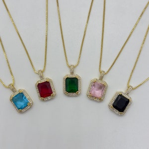Puede incluir: Cinco collares de oro con colgantes de gemas de diferentes colores. Cada colgante tiene forma rectangular con una gema transparente facetada rodeada de piedras transparentes más pequeñas. Las gemas son azules, rojas, verdes, rosas y negras.
