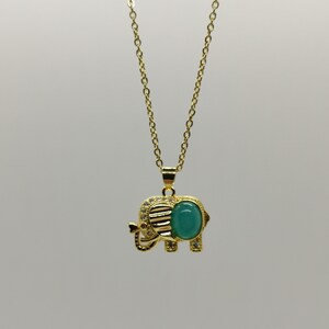May include: A gold chain necklace with a green gemstone elephant pendant. The elephant has a detailed design and is accented with small clear stones.
