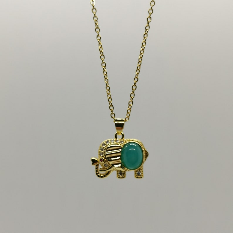 May include: A gold chain necklace with a green gemstone elephant pendant. The elephant has a detailed design and is accented with small clear stones.