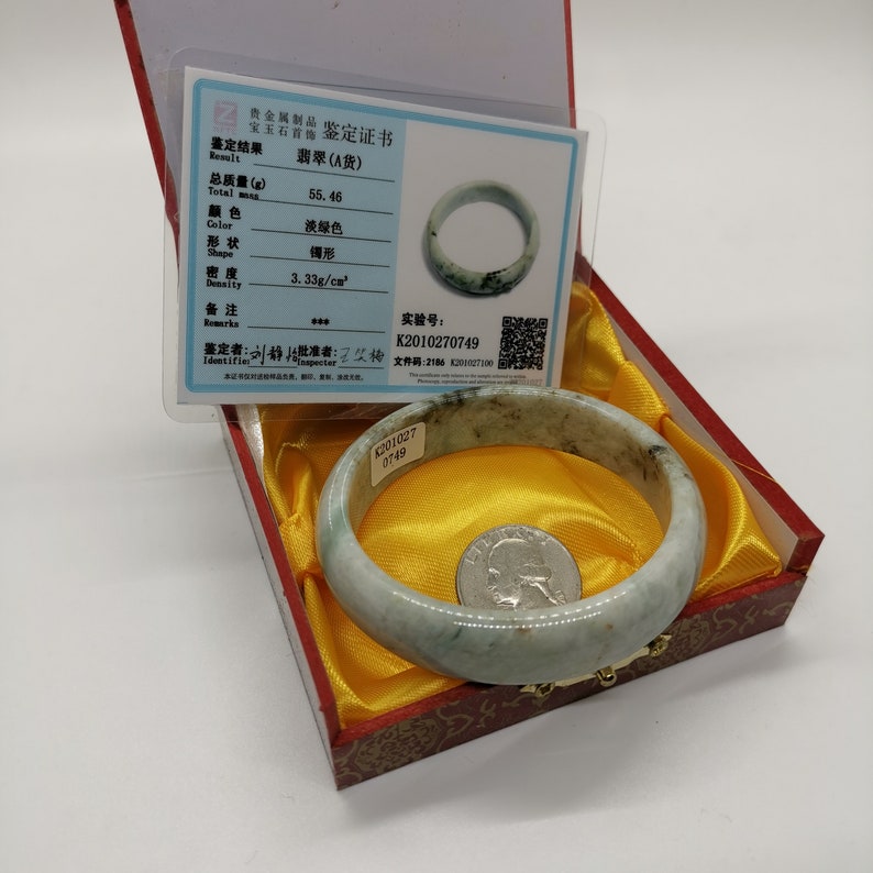 K&ouml;nnte beinhalten: Ein Jadeit-Armreif in hellgr&uuml;ner Farbe mit einem Echtheitszertifikat. Das Zertifikat besagt, dass das Gesamtgewicht 55,46 Gramm betr&auml;gt, die Farbe hellgr&uuml;n ist, die Form oval ist, die Dichte 3,33 g/cm&sup3; betr&auml;gt und die Identifikationsnummer K2010270749 lautet.