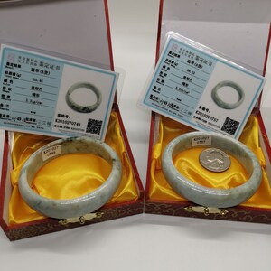 K&ouml;nnte beinhalten: Zwei Jadeit-Armreifen in roten Samtboxen mit Echtheitszertifikaten. Die Zertifikate enthalten das Gewicht, die Farbe, die Form und die Dichte jedes Armbands. Die Zertifikate enthalten auch die Versuchsnummer, K2010270749 und K2010270757.