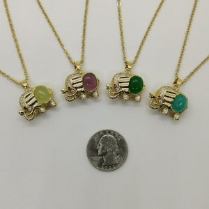 May include: Four gold elephant necklaces with different colored gemstone pendants. The pendants are green, pink, and yellow. The necklaces are on a white background.