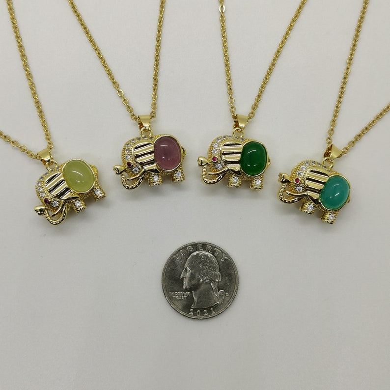 May include: Four gold elephant necklaces with different colored gemstone pendants. The pendants are green, pink, and yellow. The necklaces are on a white background.