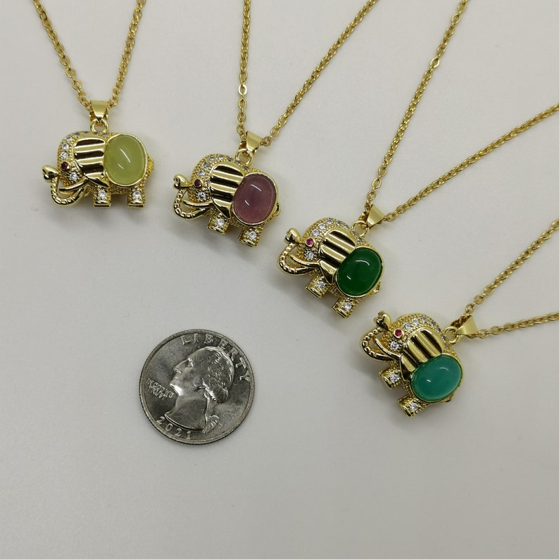 May include: Four gold elephant necklaces with different colored gemstone accents. The necklaces are on a white surface with a US quarter for scale.