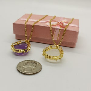 May include: Two gold heart-shaped necklaces with a purple and a white stone pendant. The necklaces are in a pink gift box with a white ribbon.
