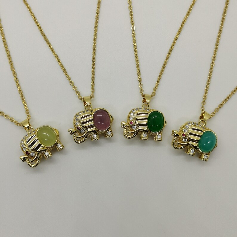 May include: Four gold elephant pendant necklaces with different colored gemstone accents. The necklaces feature a delicate chain and a small elephant charm with a gemstone in the center. The gemstones are green, pink, light green, and a darker shade of green.