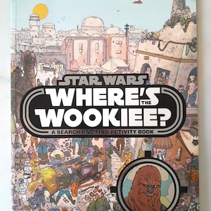 Pode incluir: Um livro de atividades Star Wars "Onde está o Wookiee?" para procurar e encontrar. A capa apresenta uma ilustração detalhada de uma cena de Star Wars com personagens e o Wookiee em uma moldura circular. O livro tem um fundo branco.