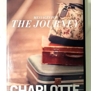 以下が含まれることがあります： シャーロット・ガンビル著「Messages for the Journey」のDVDケース。カバーには、花柄のバッグが茶色のスーツケースと青緑色のスーツケースの上に置かれ、温かみのあるセピア調の背景で積み重ねられている様子が描かれています。