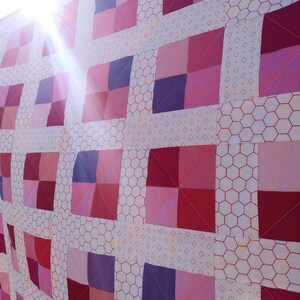 Puede incluir: Una colcha rosa y morada con un patrón de panal de abeja blanco. La colcha está hecha de cuadrados de diferentes colores y tamaños.