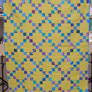 May include: A yellow quilt with a diagonal pattern of blue, green, and purple squares. The quilt is made of fabric with floral and geometric designs.