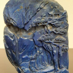 Op de afbeelding: Een blauwe lapis lazuli-carving die een berglandschap met bomen en figuren voorstelt. De carving is gedetailleerd en ingewikkeld, wat de schoonheid van de steen laat zien.