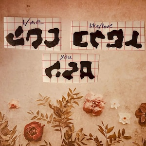 May include: Three black paper cutouts on a gridded background. The cutouts are in the shape of the words "me", "like/love", and "you".