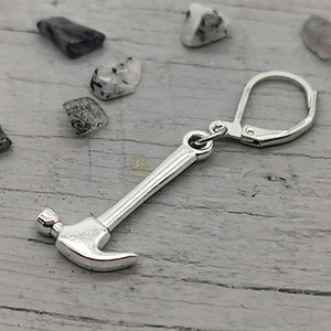May include: Silver hammer charm earring with a leverback closure. The charm is a miniature replica of a hammer with a rounded head and a long handle.