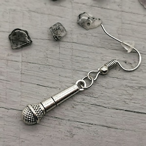 May include: Silver microphone earring with a silver hook and a clear plastic backing. The earring is on a white wooden surface.