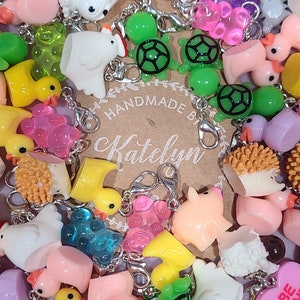 May include: A collection of colorful charms, including turtles, ducks, pigs, and a heart that says "Be Mine". The charms are made of resin and have a variety of colors and designs. The charms are attached to silver jump rings and are ready to be added to a keychain, bracelet, or necklace. Handmade by Katelyn.