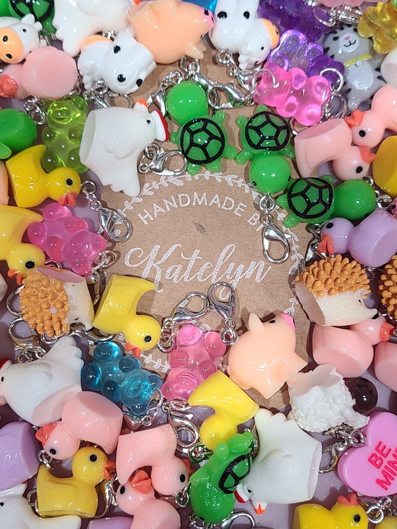 May include: A collection of colorful charms, including turtles, ducks, pigs, and a heart that says "Be Mine". The charms are made of resin and have a variety of colors and designs. The charms are attached to silver jump rings and are ready to be added to a keychain, bracelet, or necklace. Handmade by Katelyn.