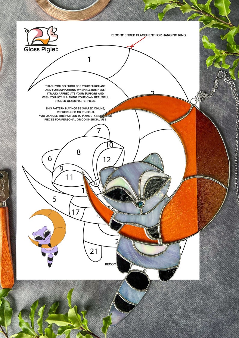 May include: A stained glass pattern for a raccoon holding a crescent moon. The pattern includes 21 numbered pieces and instructions for assembling the stained glass project. The pattern is printed on white paper with a black border.