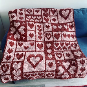 May include: A crocheted throw blanket with a repeating pattern of hearts in shades of pink and burgundy.