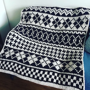 Könnte beinhalten: Schwarz-weiße gestrickte Wolldecke mit geometrischem Muster. Die Decke ist aus dickem Garn gefertigt und hat eine grobe Struktur.